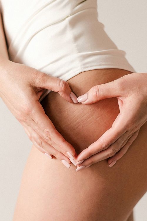 Mani che formano un cuore sulla pancia di una donna in intimo bianco, gesto affettuoso.